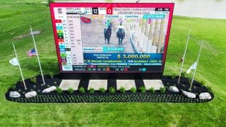 A large, vibrant video board is nestled in a manicured garden of dark mulch, green plants, and gray stone.